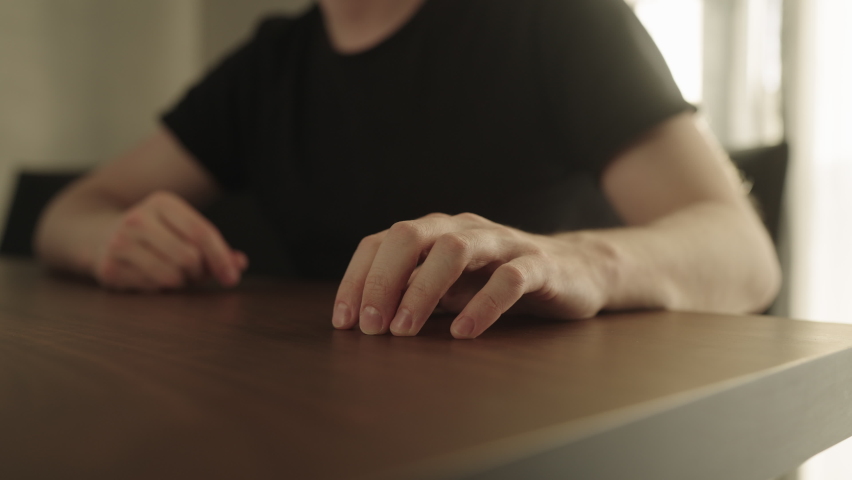 Man sitting in a chair and finger tapping on a walnut table with bright sunlight from a window behind