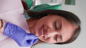 Vertical video Woman Professional Dentist Examines a Smiling Female Patient in a Dental Clinic. Selects the Shade of Dental Implants Before Operation. Concept of Healthcare and Medicine. Slow Motion.