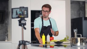 Man chef food blogger in black apron looking camera and cooking in home kitchen. Chef have online master class cutting vegetables ingredients cooking salad on table. Realtime