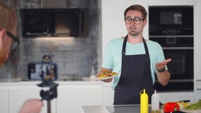 Food blogger cooking fresh vegan meal in kitchen studio, filming tutorial. Male influencer talks about healthy eating on camera. Chef make cooking video. Realtime