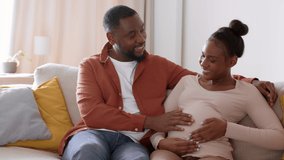 Happy pregnancy. Young positive african american man caressing big belly of his pregnant wife, discussing their parenthood, resting together on sofa, tracking shot, slow motion, empty space - Powered by Shutterstock - Get 15% off with code: PIKWIZARD15