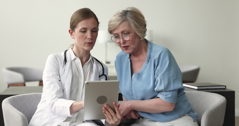 GP holding tablet showing health test check up result, share treatment plan with older woman during appointment in private clinic, patient getting professional medical services. Modern tech, medicine Royalty-Free Stock Footage #1097844993