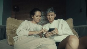 Two young women sitting with their phones on the couch in their home