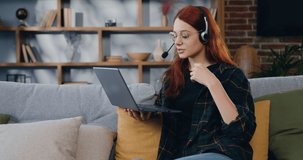 Young woman in headphones, talking video call, sitting on the sofa at home. Online education, distance training, business meeting, webinar conference.