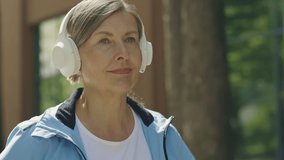 Portrait of the smiled mature woman running outside wearing headphones. Sporty mature woman wearing headphones while running. Sport and healthy lifestyle concept. Aging Youthfully - Powered by Shutterstock - Get 15% off with code: PIKWIZARD15