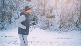 Adult man is jogging in park in winter. 4K video.