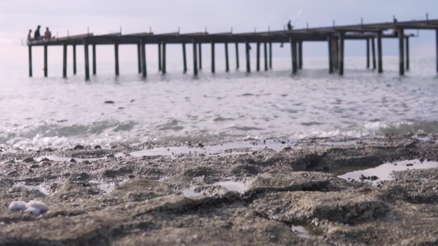 Fishermen fish on a pier in the sea, the bridge is blurred, the focus on the rocks and the sea is in the foreground.
