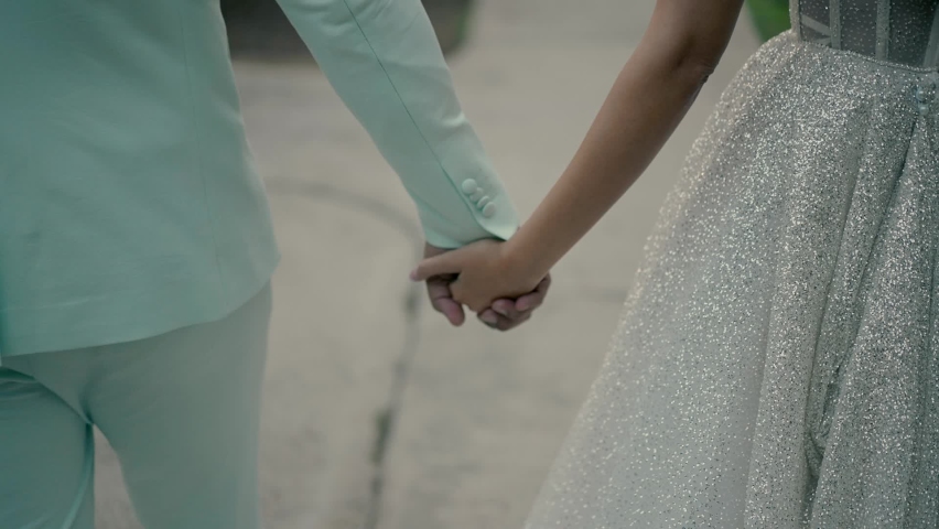 the bride and groom walking along the path in the garden hold hands
