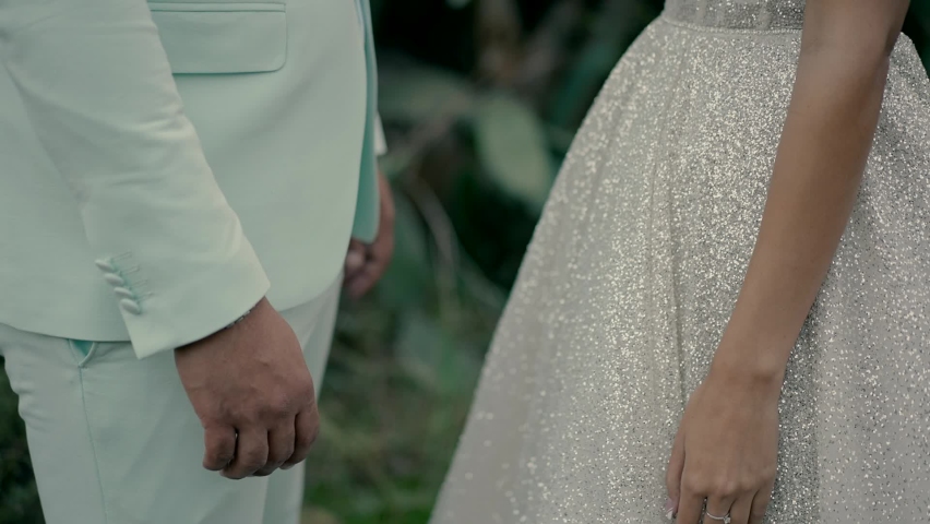 the bride and groom standing opposite each other in an open area join hands.