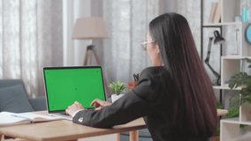Asian Businesswoman Wearing Business Suit Talking On Green Screen Computer While Working At Home
