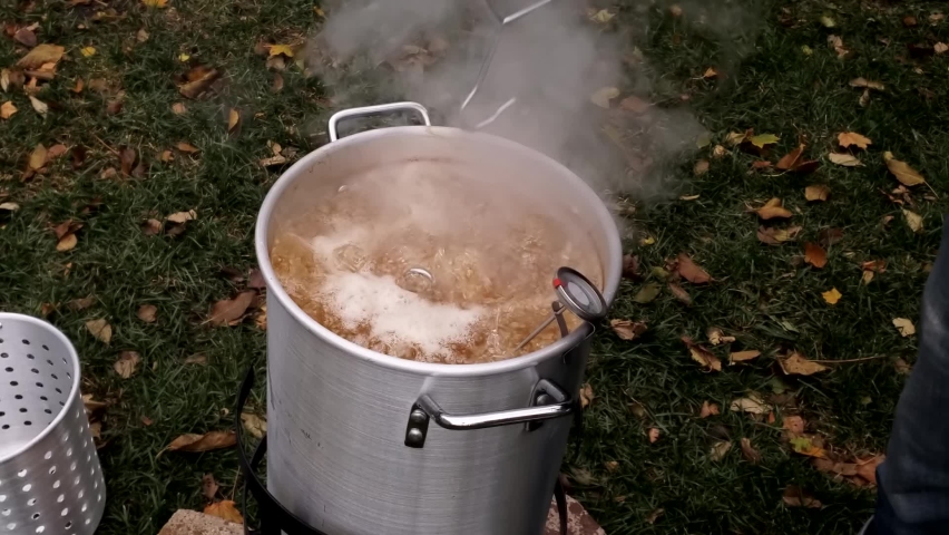 Checking large turkey being deep fried in peanut and soy oil blend in large pot at back yard. Royalty-Free Stock Footage #1097871431