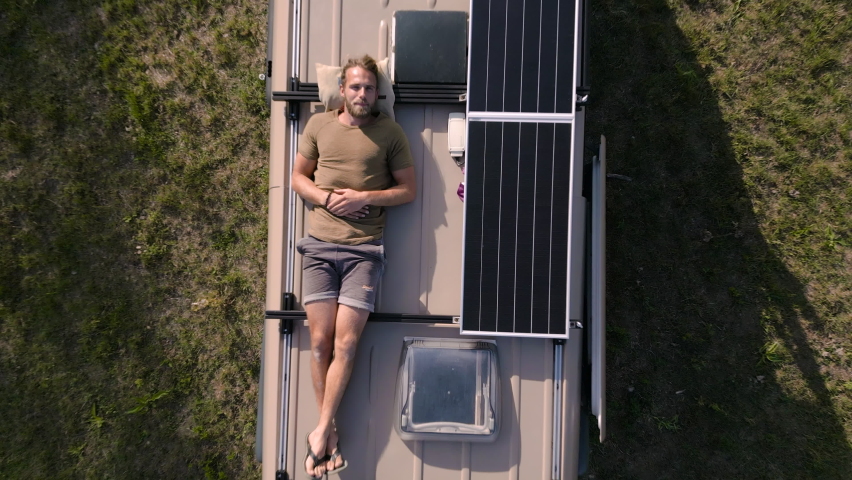 Aerial shot of a man relaxing on the roof of a camper van Royalty-Free Stock Footage #1097872877