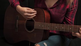 Guitarist plays acoustic guitar at home. The woman strums the chords on the frets and plays the song. Learning to play the classical guitar. Young musician playing guitar in the living room at home