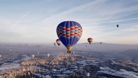 Aerial drone video of famous Hot air balloons flying over beautiful Cappadocia, Göreme, Turkey during the amazing sunrise in a snowy winter day.