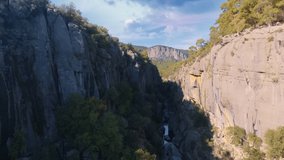 Flight between rocks in a mountain gorge. Drone video footage. Green plants on gray rocks. Canyon