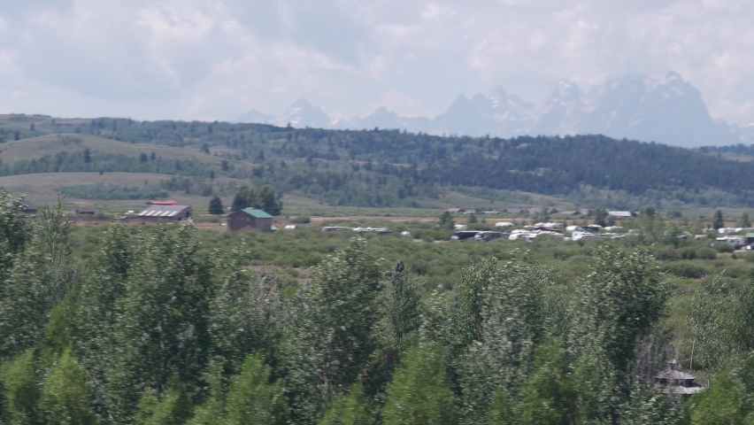 Aerial in front of pine trees and rural ranch land in Moran, Wyoming with Grand Tetons in background