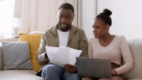 Family budget problems. Irritated african american man and woman accounting finances, checking bills on papers and laptop, sitting at home, tracking shot, slow motion, empty space