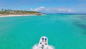 Speedboat with two people on board sailing on turquoise ocean waters of Playa Blanca beach, Punta Cana in Dominican Republic. Aerial tracking