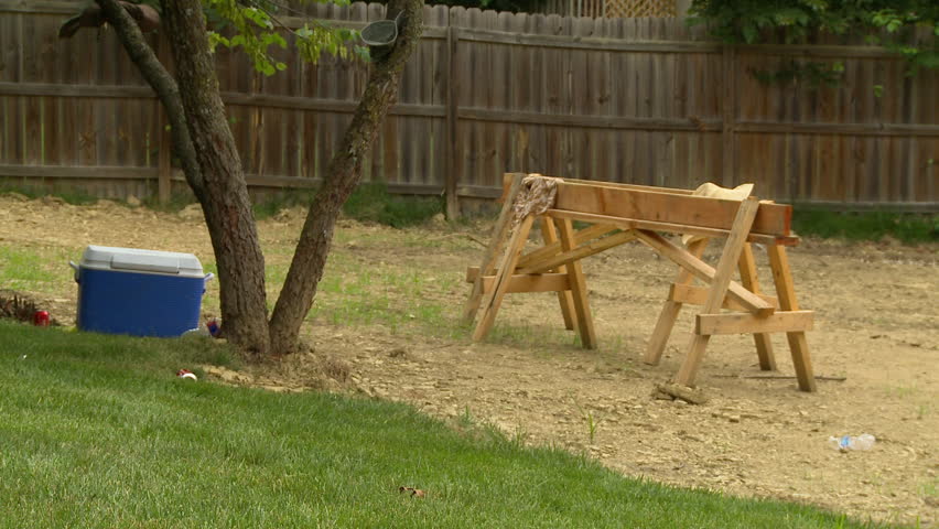 A wooden saw horse work bench and blue cooler sit under a shade tree.