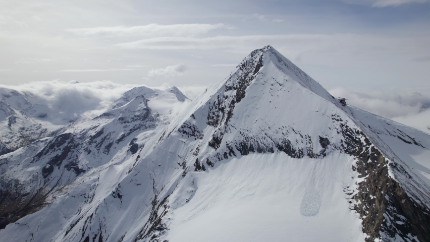 Cinematic drone shot of snowy mountain summit during sunny day in austrian Alps