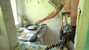 Smartphone On Tripod Filming A Man Cooking In Small Kitchen In The House. selective focus