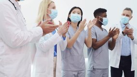 Multiethnic group of happy professional medical workers applauding after successful surgery. Young beautiful doctors wearing medical apparel and masks clapping hands. Medical service concept. - Powered by Shutterstock - Get 15% off with code: PIKWIZARD15
