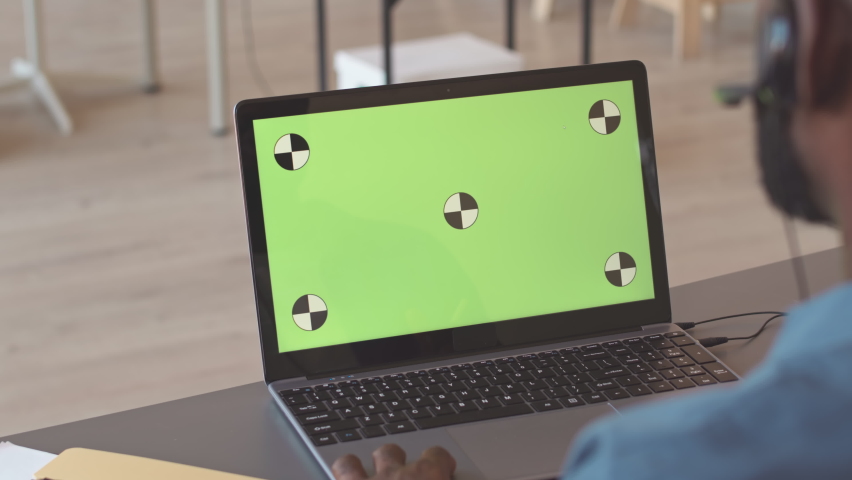 Back view of African American male call centre operator in headset microphone looking at copy space laptop screen while consulting clients