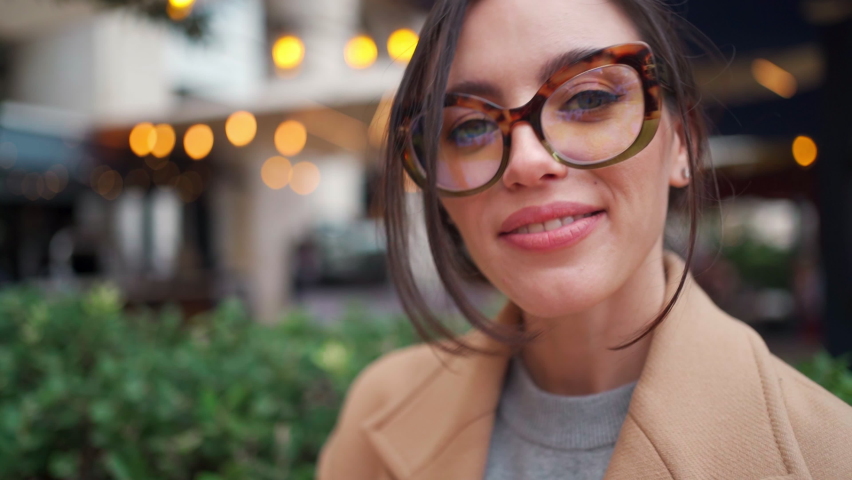 Close up Portrait Caucasian brunette Woman in eyeglasses. Smiling Adult Elegant Lady wears Coat standing outdoors correct glasses by hand. Stylish person in glasses middle shoot teeth gummy smile Royalty-Free Stock Footage #1097909779