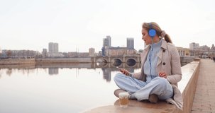 A young woman in headphones and listens to relaxing music on the embankment. Rest from office bustle and city noise. 4k footage. Slow motion.