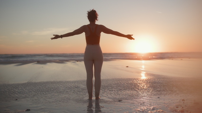 Seen from behind fitness woman jogger in fitness clothes at the beach at sunset meditating.