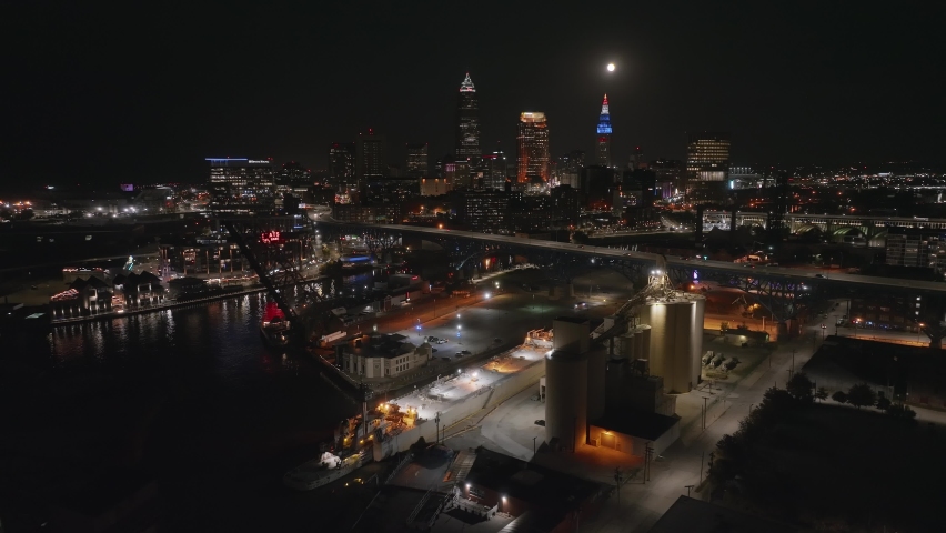 Wide aerial nighttime orbit shot of Cleveland Ohio skyline with the Flats in foreground and full moon above city in background Royalty-Free Stock Footage #1097912885
