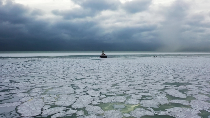 Aerial view over ice blocks towards Chicago Harbor Lighthouse, dramatic, winter day on Lake Michigan