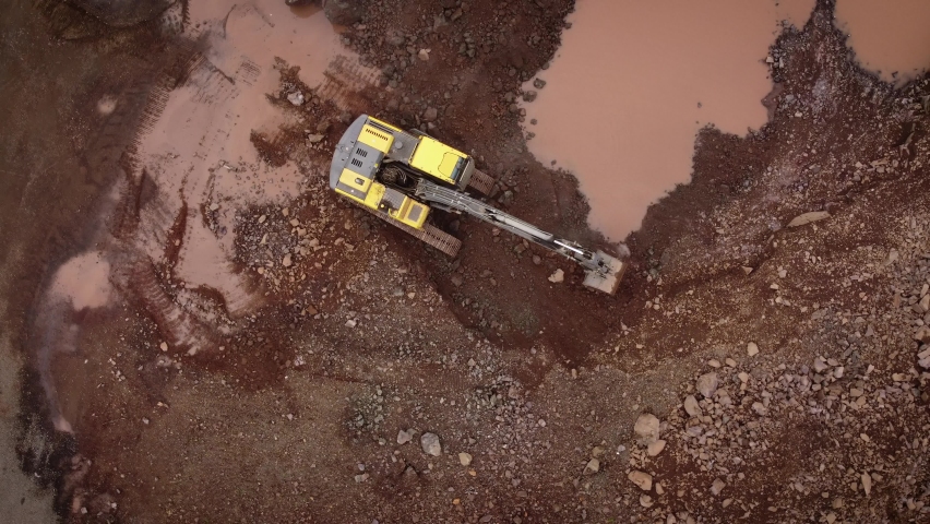 A dynamic top-down aerial footage of an excavator in action while working on a quarry site to move dirt and rocks away.