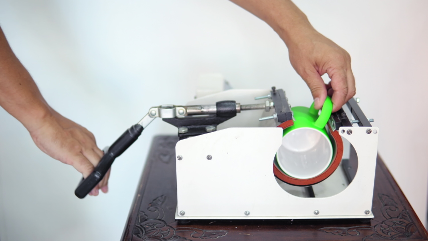 Man putting mug in a thermopress for cup print - intended for transfer image or a logo on a mug, cup
