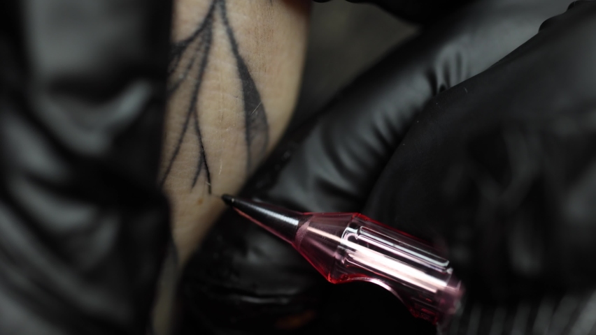 Macro video of a young professional tattoo master introduces black ink into the skin using a needle from a tattoo machine. Tattoo on hand close-up Royalty-Free Stock Footage #1097917027