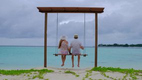 Couple is on swings. Man and woman is happy on Maldives. Blue turquoise ocean on the background. Girl enjoys her tropical holidays. Summer travel vacation concept. Slow motion 4k video.