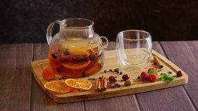 Preparing fruit tea, woman's hand putting orange slices, cranberries, cinnamon sticks into glass teapot placed on tray, hot spiced winter drink, Christmas recipe, 4k video clip