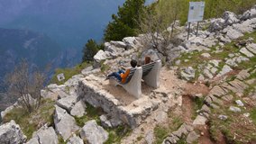 Aerial video of a family of tourists visitng the Grlo Sokolovo canyon a famous sightseeing location in Montenegro. They sit on a bench with a breathtaking view on the canyon