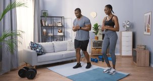 Full length view of the strong active multiracial couple doing lunges while training at their cozy apartments with pleased emotions. Stock video
