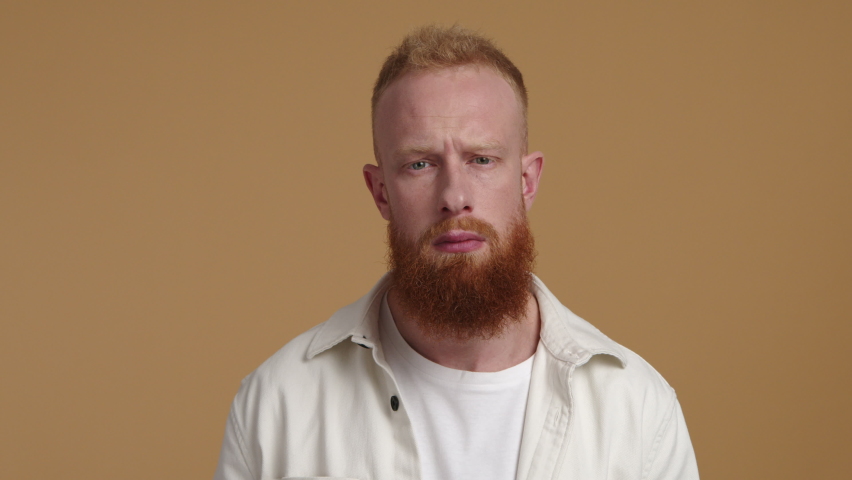 Close-up view of a male casual clothes making subordinate gesture. Redhead man with beard saluting with isolated, yellowish background. High quality 4k footage