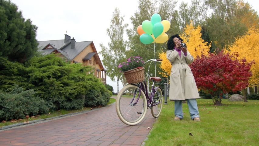 Young woman with curly, ethnic hair having adventurous, weekend ride along park lanes. Female photographer taking pictures with a retro-styled camera outdoors. High quality 4k footage