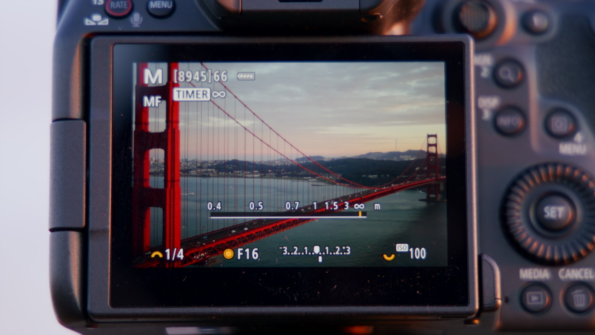 Beautiful sunset views over calm ocean waters of the Bay Area in San Francisco. Close-up view of professional camera taking photos of iconic Golden Gate Bridge. High quality 4k footage