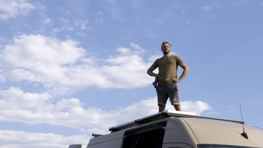 Man proudly standing on top of his camper van while looking into the distance