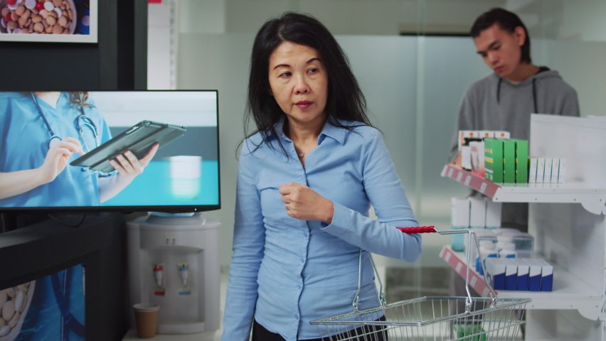 Asian customer asking pharmacist for help with medicaments, sarching for prescription medicine in bottle. Consultant checking supplement and plls boxes to give treatment to person.