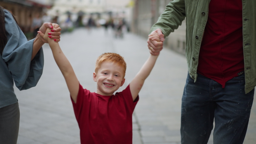 Youg parents with their little redhead son walking in the city.