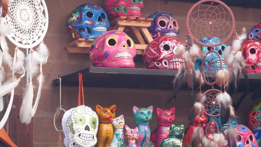 Mexican souvenirs on market stall, colorful painted skulls and dream catchers. Multicolor vivid ethnic ornaments, bazaar or marketplace. Ceramic crafted death symbol for sale on counter. Day of Dead. Royalty-Free Stock Footage #1097945263