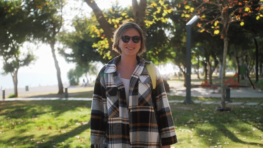 Portrait of beautiful young woman with short hair wearing sunglasses, looking up to the camera and smiling charmingly.
