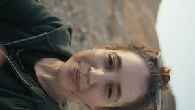 Vertical video - Young woman traveler talking on video call with smartphone. Female in desert scenery smiling and showing to camera where she is. Waving speaking during remote conversation in nature