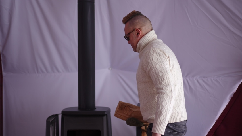 Confident man putting firewood closing furnace talking to blurred woman smiling. Portrait of Caucasian husband chatting with wife resting in eco hotel room. Lifestyle and leisure