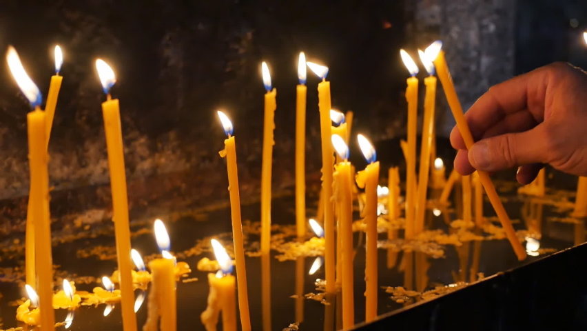 Human hands light candles in the temple on the altar and insert them while standing. The concept of faith in god and asking for help from the Almighty with the help of prayer in the temple Royalty-Free Stock Footage #1097951263